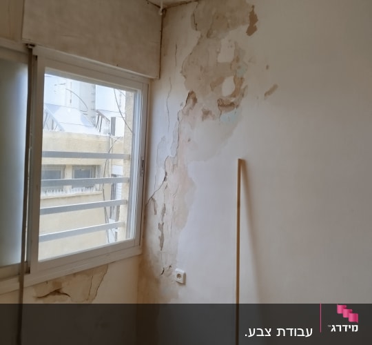 קיר עם קילופי צבע ותקרה פגומה ליד חלון